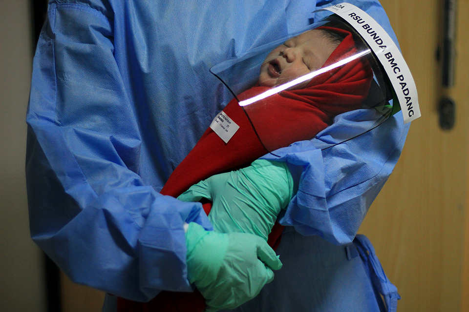 MASKER PELINDUNG WAJAH - Perawat menggendong setelah memasangkan pelindung wajah versi kecil untuk bayi yang baru dilahirkan di Unit Ibu dan Anak RS BMC Padang, Sabtu (18/4/2020). Bayi yang baru lahir di RS tersebut dipakaikan alat pelindung diri berupa face shield, sebagai upaya pencegahan penyebaran virus corona (Covid-19). Menurut pejabat dirumah sakit itu, selama pandemi, jumlah peserta BPJS lebih mendominan untuk berobat ke RS tersebut dibandingkan yang tidak peserta. Hal itu membuktikan bahwa pelayanan fasilitas kesehatan untuk peserta JKN-KIS dimasa pandemi tetap berjalan. (givo alputra)